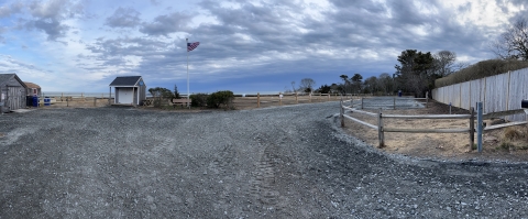 a freshly completed gravel lot at a national wildlife refuge. A flag pole, fencing, and small shed-like buildings are seen in the background