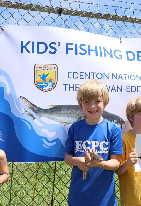 3 children in front of kids fishing derby banner at Edenton National Fish Hatchery