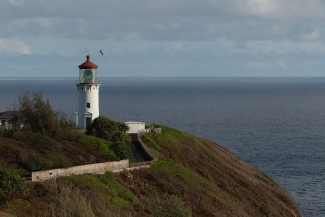 photo of a lighthouse on a bluff looking over the ocean. There is a paved path leading up to it. 