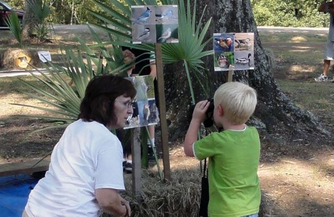 A woman kneels to be at eye level with a child looking through binoculars at an Outreach Event at Tensas Refuge
