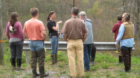 Female biologists speaking to six other individuals who surround her