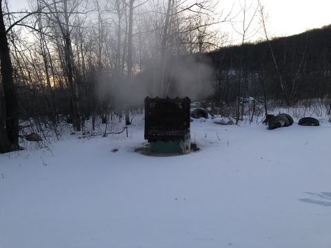 Steam floating out of a ground vent that is surrounded by snow.