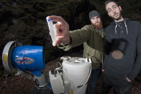Biologists hold up a vial of chemicals before placing it in a mosquito fogger.