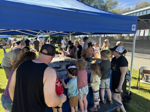 Kids and adults gather around a water table filled with sand and toys