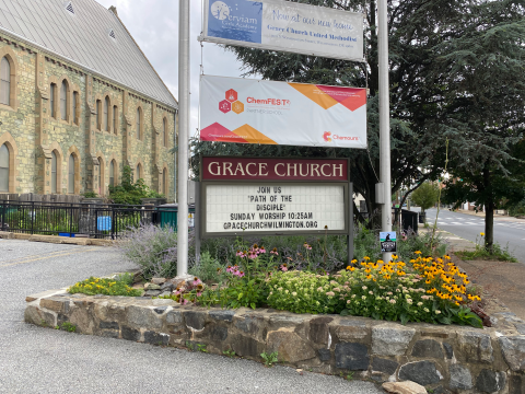 A sign for a church in a city surrounded by a garden be full of blooming flowers